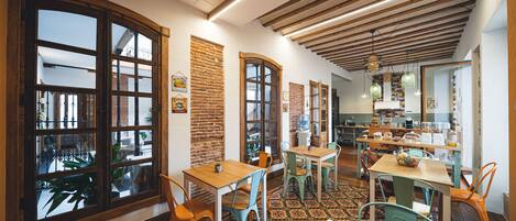 A restaurant with wooden tables and chairs, large windows, and a brick wall.