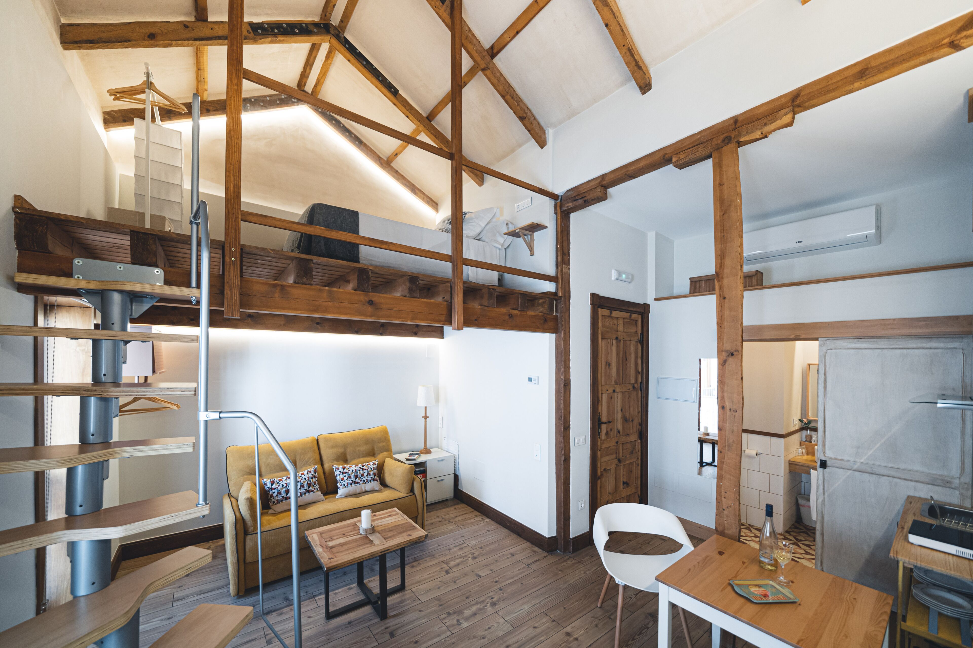 Una habitación compacta y rústica con cama en altillo, sofá, mesa de comedor y zona de cocina.