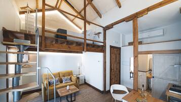 Una habitación compacta y rústica con cama en altillo, sofá, mesa de comedor y zona de cocina.