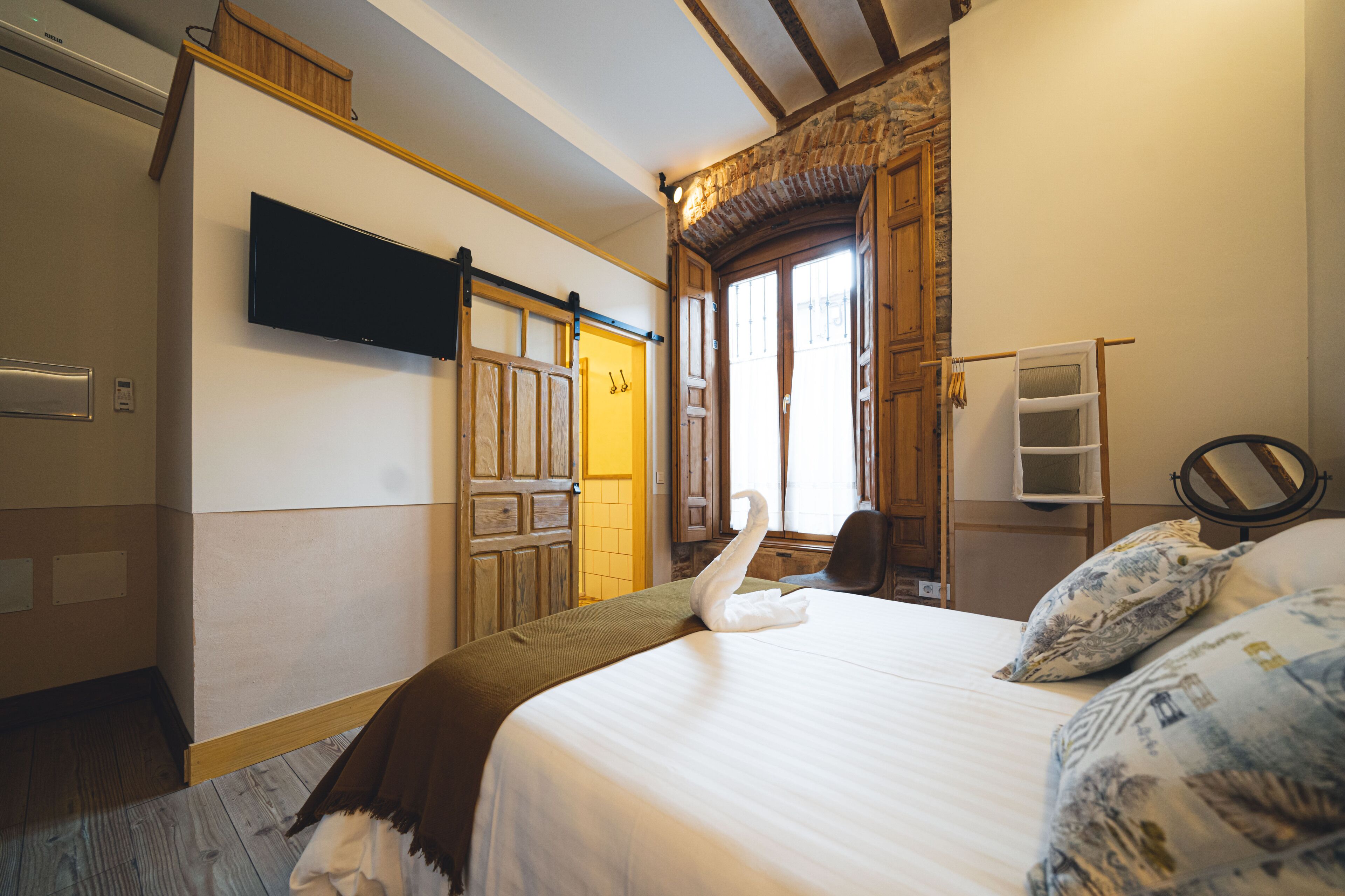 Une chambre d’hôtel avec un lit, un téléviseur à écran plat fixé au mur, des portes en bois et une fenêtre donnant sur un paysage agréable.