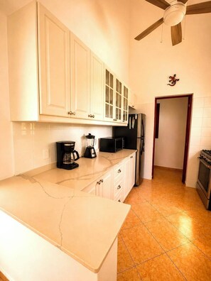 A kitchen with white cabinets, a coffee maker, a refrigerator, and a stove.