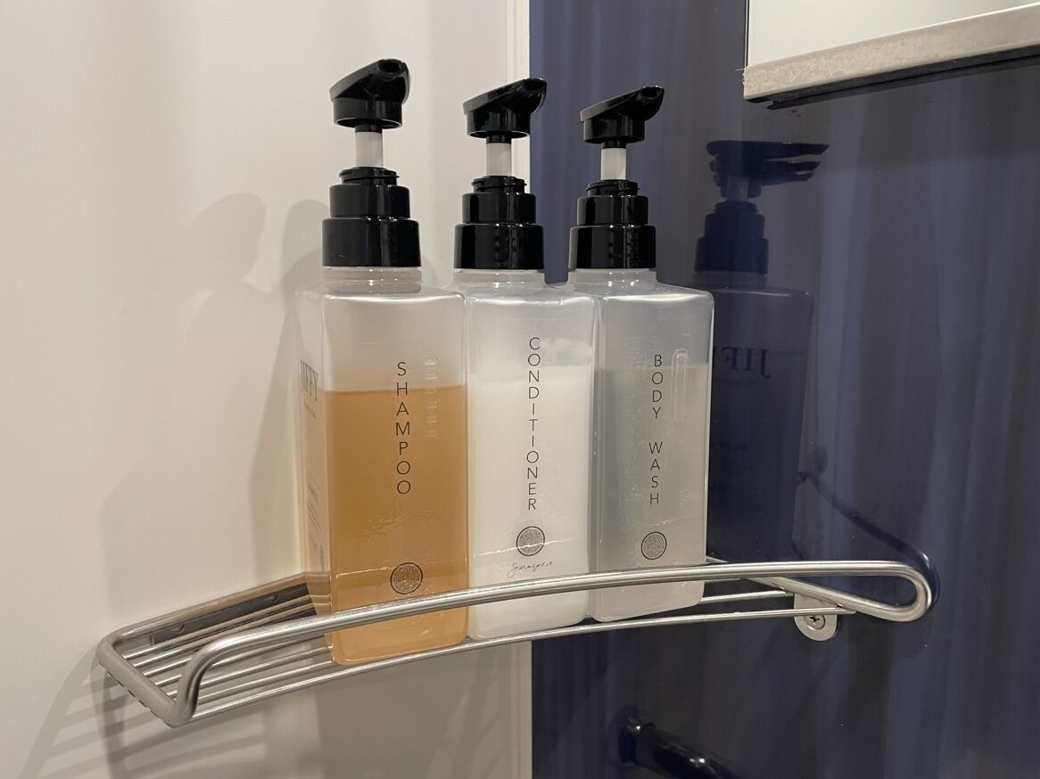 Un estante con tres botellas de champú, acondicionador y gel de baño.