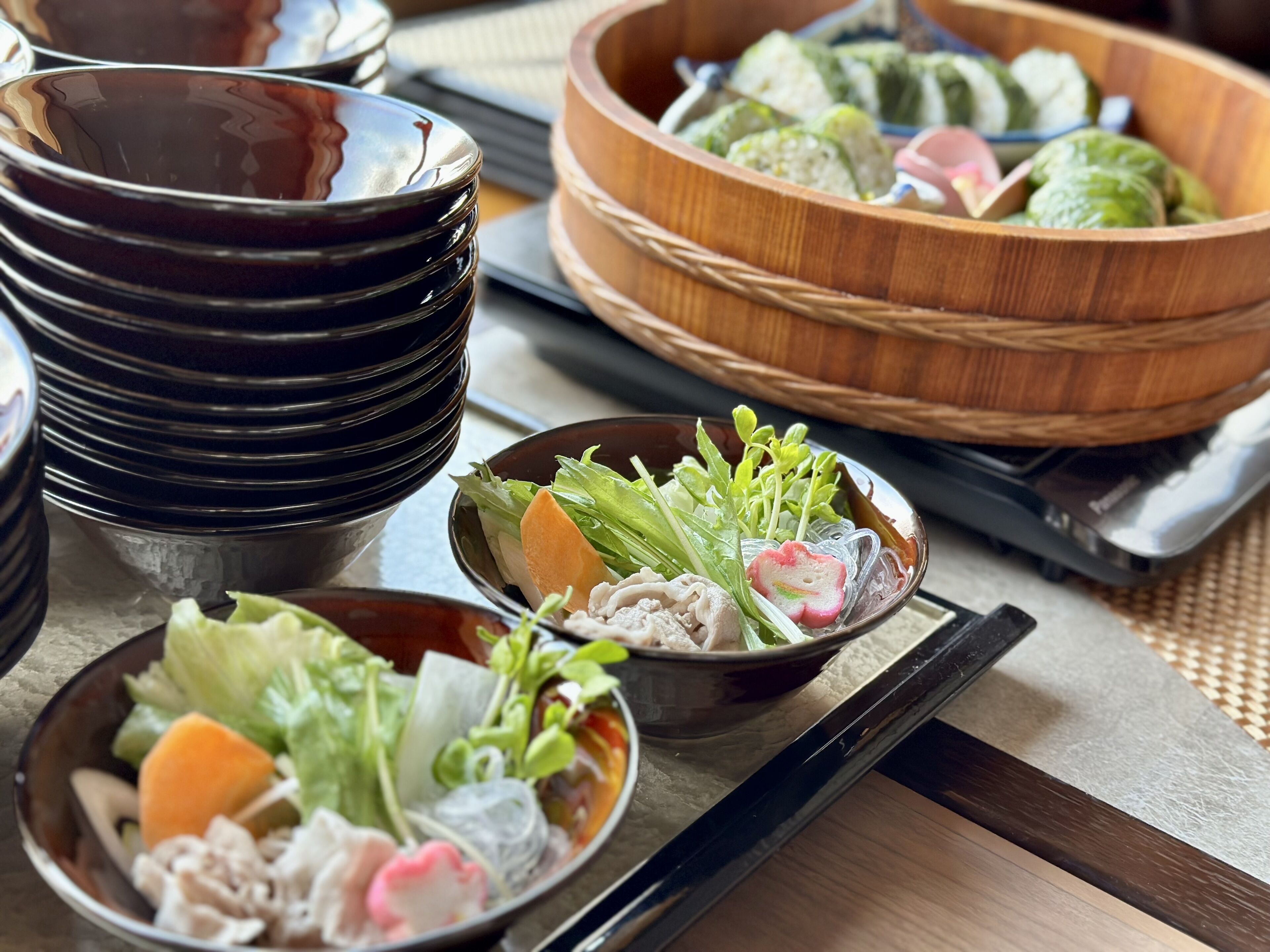 A table with various dishes, including a bowl of salad, a bowl of dumplings, and a stack of black bowls.