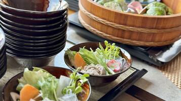A table with various dishes, including a bowl of salad, a bowl of dumplings, and a stack of black bowls.