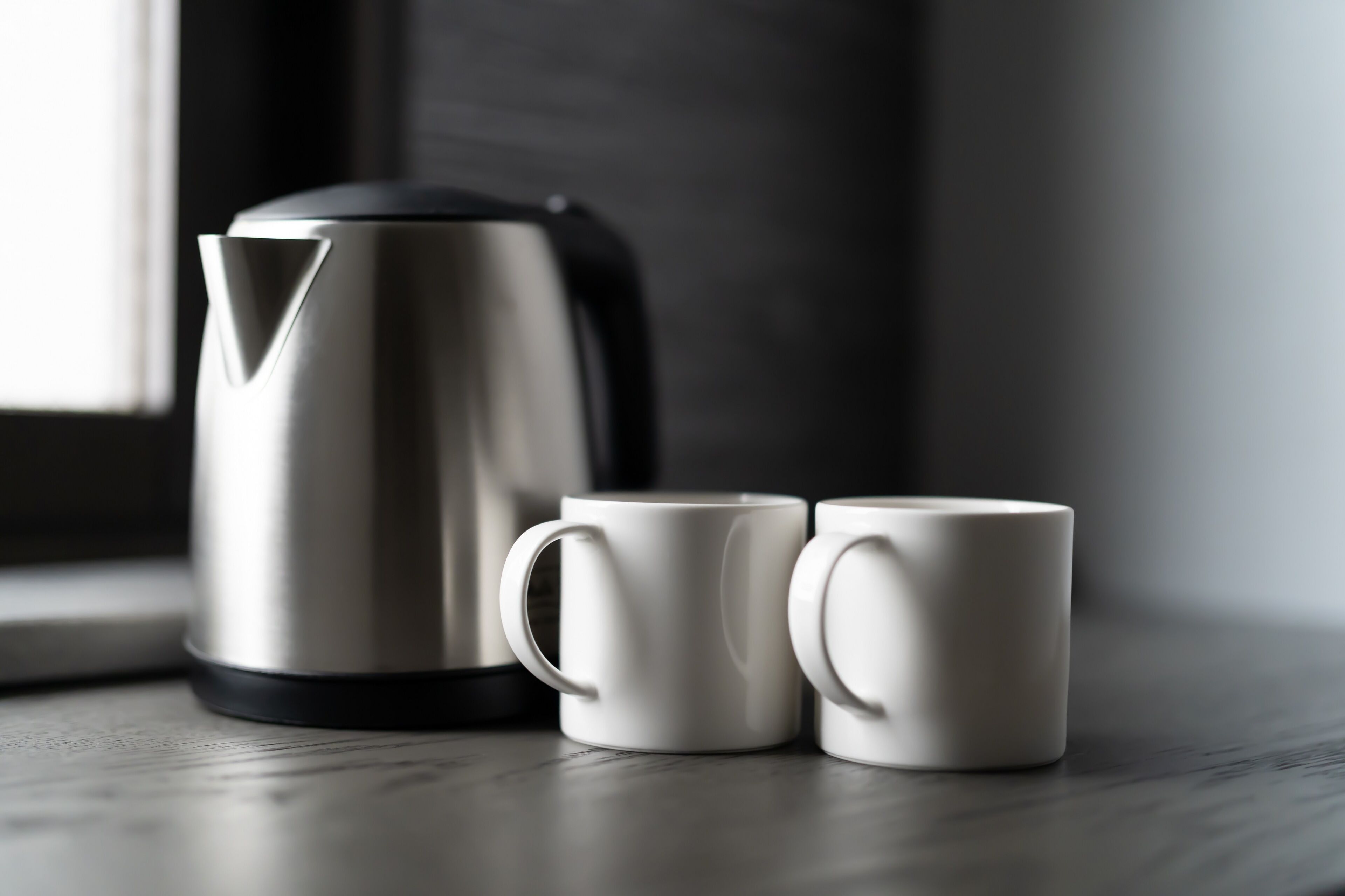 Una tetera de acero inoxidable y dos tazas blancas sobre una superficie de madera.