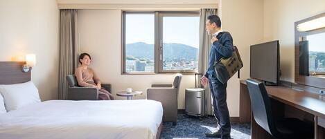 Habitación de hotel con cama, escritorio, silla, televisión y vistas a la ciudad y montañas.