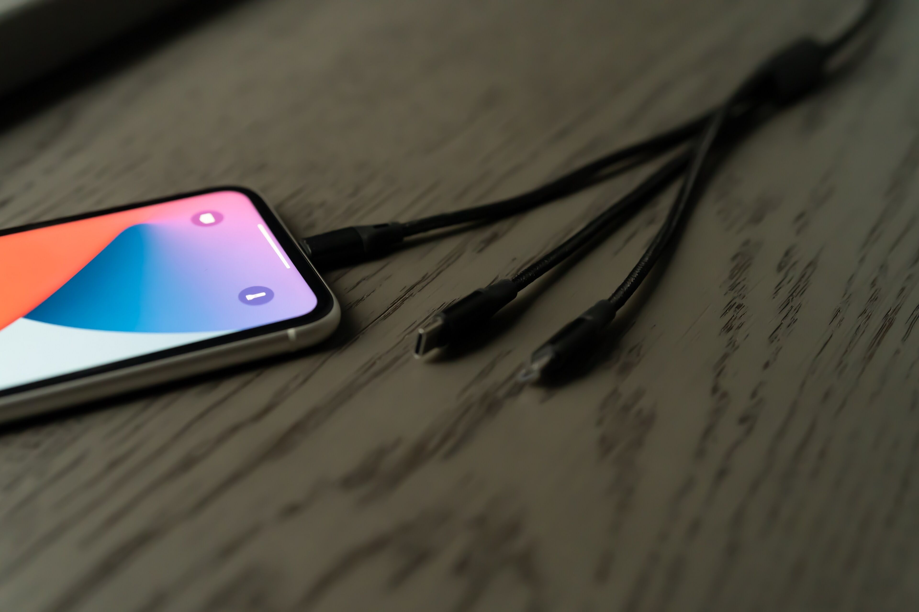 Un teléfono inteligente con una pantalla colorida y cables de carga sobre una superficie de madera.