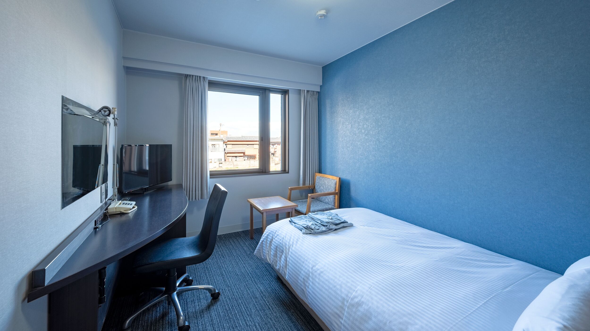 Habitación de hotel con cama, escritorio con televisor, silla y ventana con cortinas.