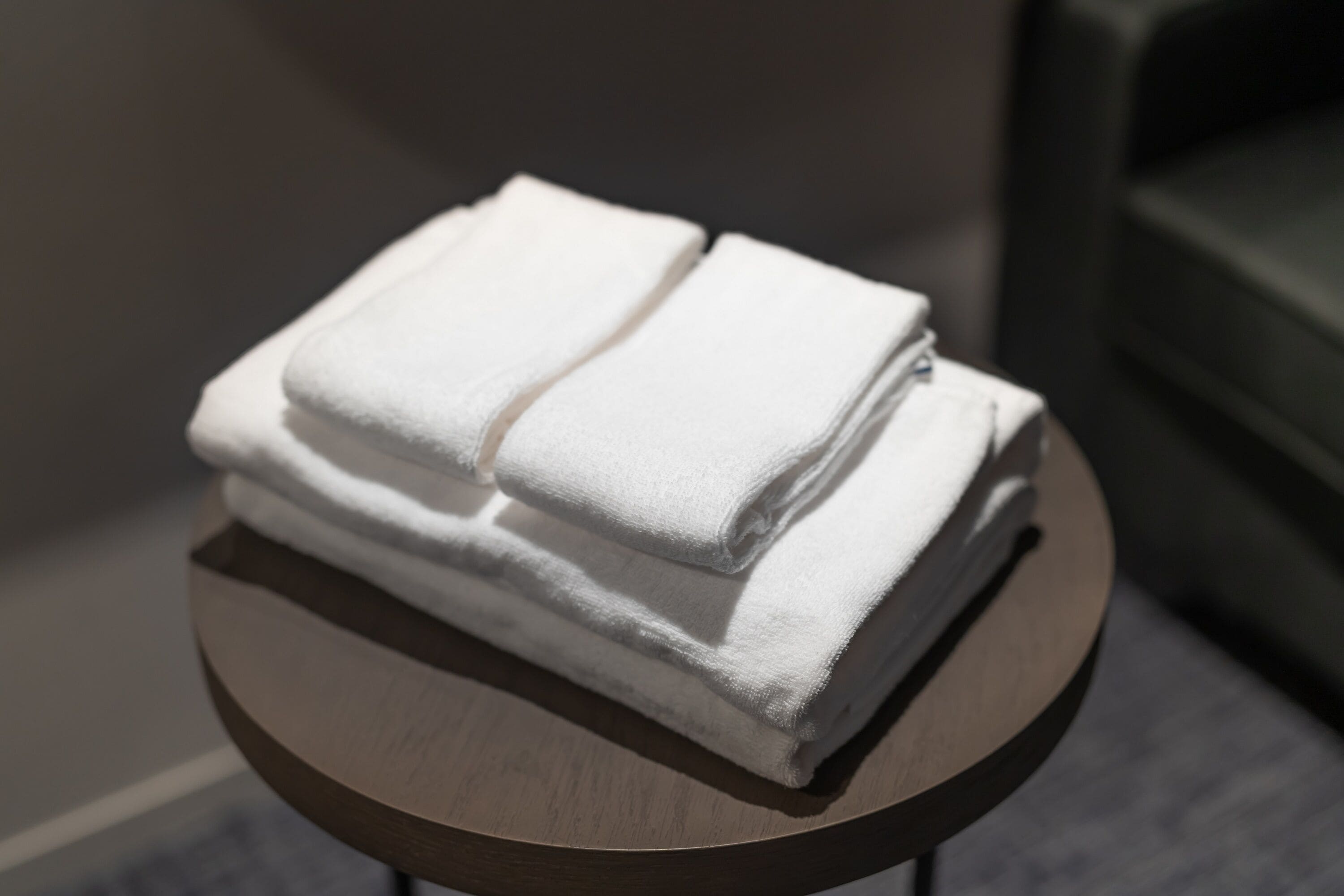 A stack of white towels on a round wooden table in a hotel room.