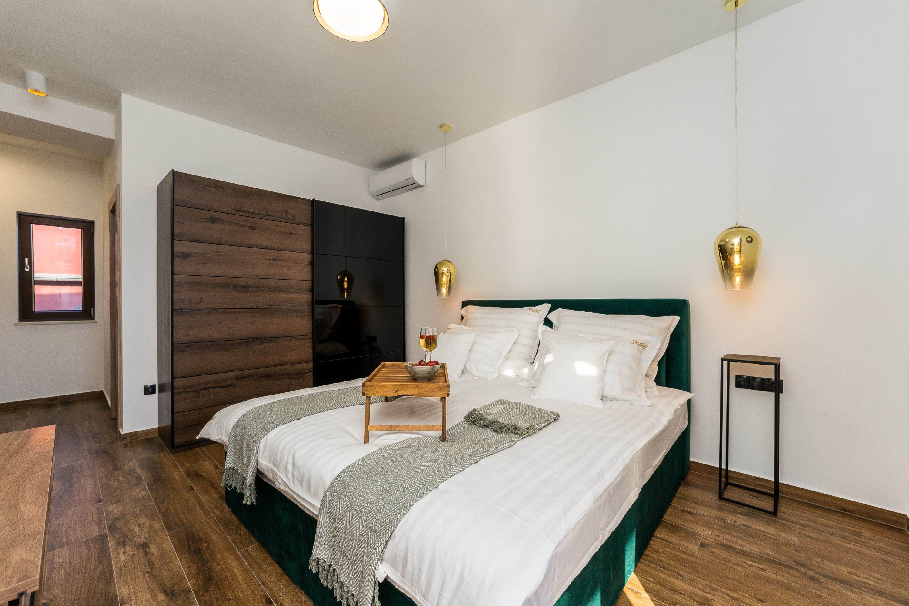 Een moderne slaapkamer met een groot bed, een houten nachtkastje, een klein bijzettafeltje en een wandlamp.