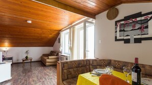A dining area with a table set for two, a sofa, and a window with curtains. - Breathtaking View - Attic Apartment (Dubrovnik)