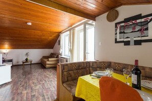 Un coin repas avec une table dressée pour deux personnes, un canapé et une fenêtre avec des rideaux.