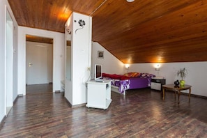 A room with a sloped ceiling, a bed with a purple bedspread, a desk with a computer, and a small table with a plant. - Breathtaking View - Attic Apartment (Dubrovnik)