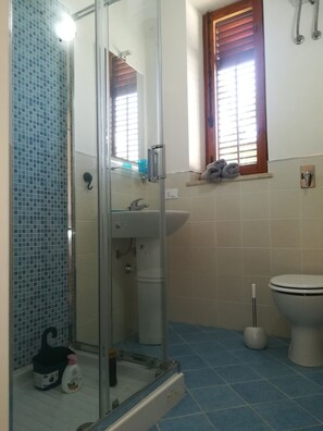 A bathroom with a glass shower enclosure, a sink, a toilet, and a window with blinds. - Casa Maria & Bartolomeo (Marsala)