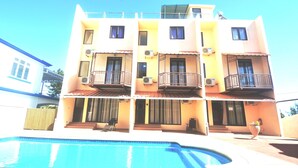 A multi-story building with balconies, a swimming pool, and a clear sky.