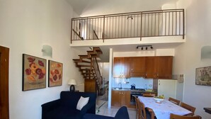 A living room with a sofa, a dining table with chairs, a kitchen area with wooden cabinets, and a staircase leading to an upper level. - Fabulous Apartment in the Historic Center, Bright and With Easy Parking (Spoleto)
