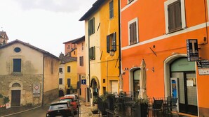 A narrow street with parked cars, a building with a sign for a tobacconeria, and a stone wall with a circular window. - Fabulous Apartment in the Historic Center, Bright and With Easy Parking (Spoleto)