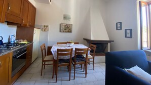 A kitchen with wooden cabinets, a stove, and a dining table with chairs. There is a fireplace and a window with curtains. - Fabulous Apartment in the Historic Center, Bright and With Easy Parking (Spoleto)