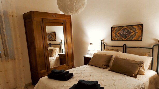 A bedroom with a bed, a nightstand, a mirror, a lamp, and a painting on the wall. - Fabulous Apartment in the Historic Center, Bright and With Easy Parking (Spoleto)