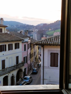 A narrow street lined with buildings, a car parked on the side, and a view of the distant hills. - Fabulous Apartment in the Historic Center, Bright and With Easy Parking (Spoleto)