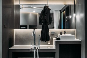 Un baño moderno con un espejo grande, un lavamanos, una bata colgada en la pared y un perchero para toallas.