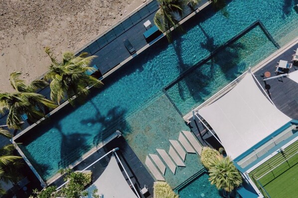 An aerial view of a resort with a clear blue pool, palm trees, and a sandy beach. - Hotel Tide Phuket (Ratsada)