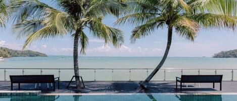 Une piscine avec deux bancs et des palmiers, donnant sur une mer calme.