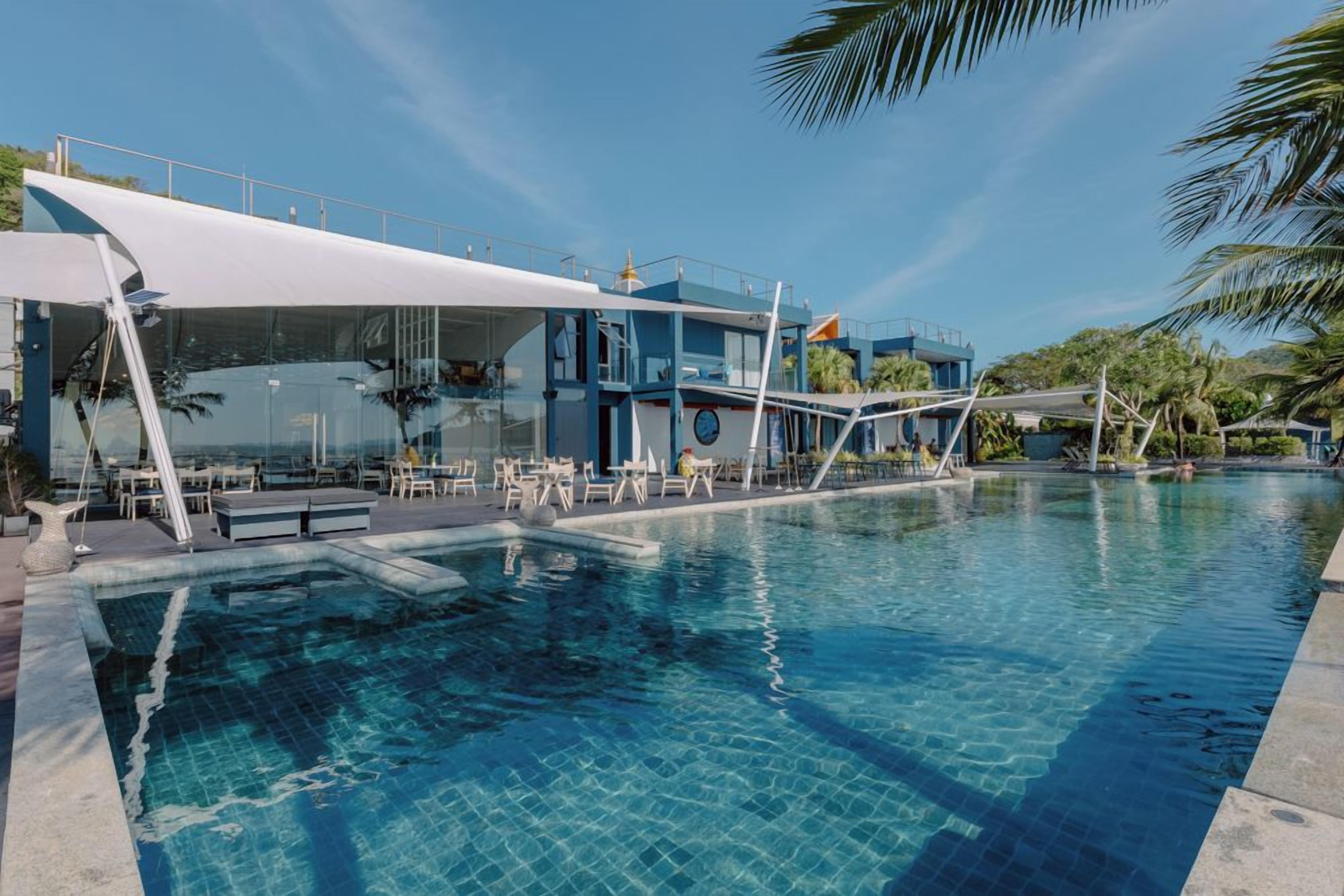 Una piscina con un edificio moderno contiguo, que cuenta con asientos exteriores y una zona cubierta.