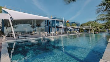 Una piscina con un edificio moderno contiguo, que cuenta con asientos exteriores y una zona cubierta.
