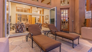 Un espace aménagé au bord de la piscine, avec des chaises longues, une table et un bar, visible à travers une porte ouverte.
