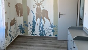 Una stanza con pavimento in legno, una porta bianca e un muro decorato con un murale a tema naturalistico, raffigurante cervi e alberi.