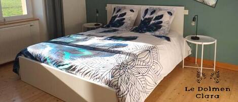 A bedroom with a bed, two bedside tables, a window, and artwork on the wall.