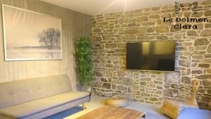 Un soggiorno con parete in pietra, televisione a schermo piatto, divano, tavolino da caffè e un quadro.