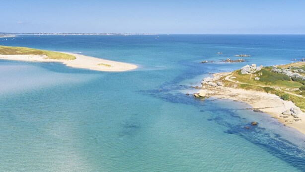 Una vista aerea di una zona costiera con acque blu cristalline, spiagge sabbiose e affioramenti rocciosi.