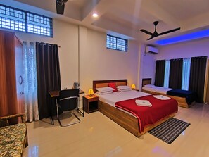A hotel room with a large bed, a desk, a chair, a small table, and a ceiling fan. - Hotel Residence Park (Tezpur)