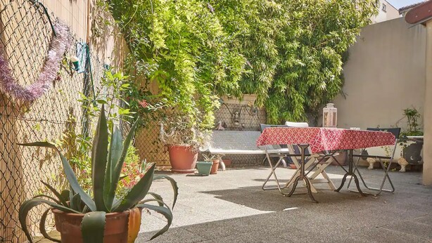 A patio area with a table and chairs, surrounded by potted plants and a chain-link fence. - Charming town house very close to Paris. (Pantin)