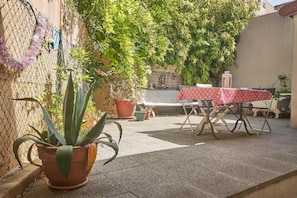A patio area with a table and chairs, surrounded by potted plants and a chain-link fence.