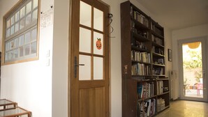 A hallway with a wooden door, a bookshelf filled with books, and a small table. - Charming town house very close to Paris. (Pantin)