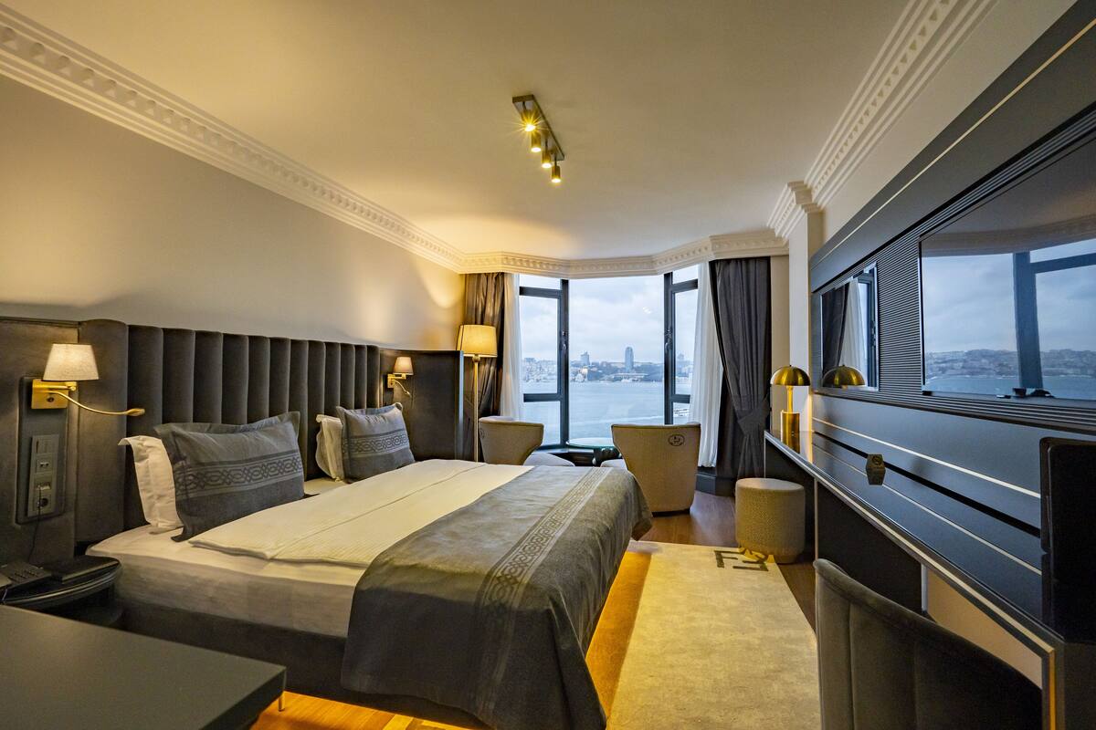 A hotel room with a large bed, a desk, a TV, and a view of the city.
