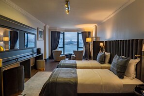 A hotel room with two beds, a desk, a chair, a small table, and a view of the city through large windows. - A11 Hotel Bosphorus (Istanbul)