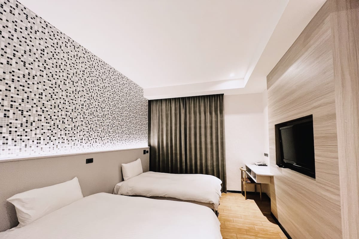 Una habitación de hotel moderna con dos camas, un televisor grande montado en la pared y un escritorio con teléfono.