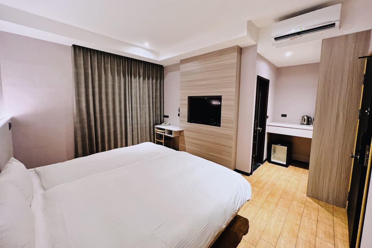 Habitación de hotel con una cama grande, un escritorio con silla, televisor montado en la pared, lavamanos y unidad de aire acondicionado.