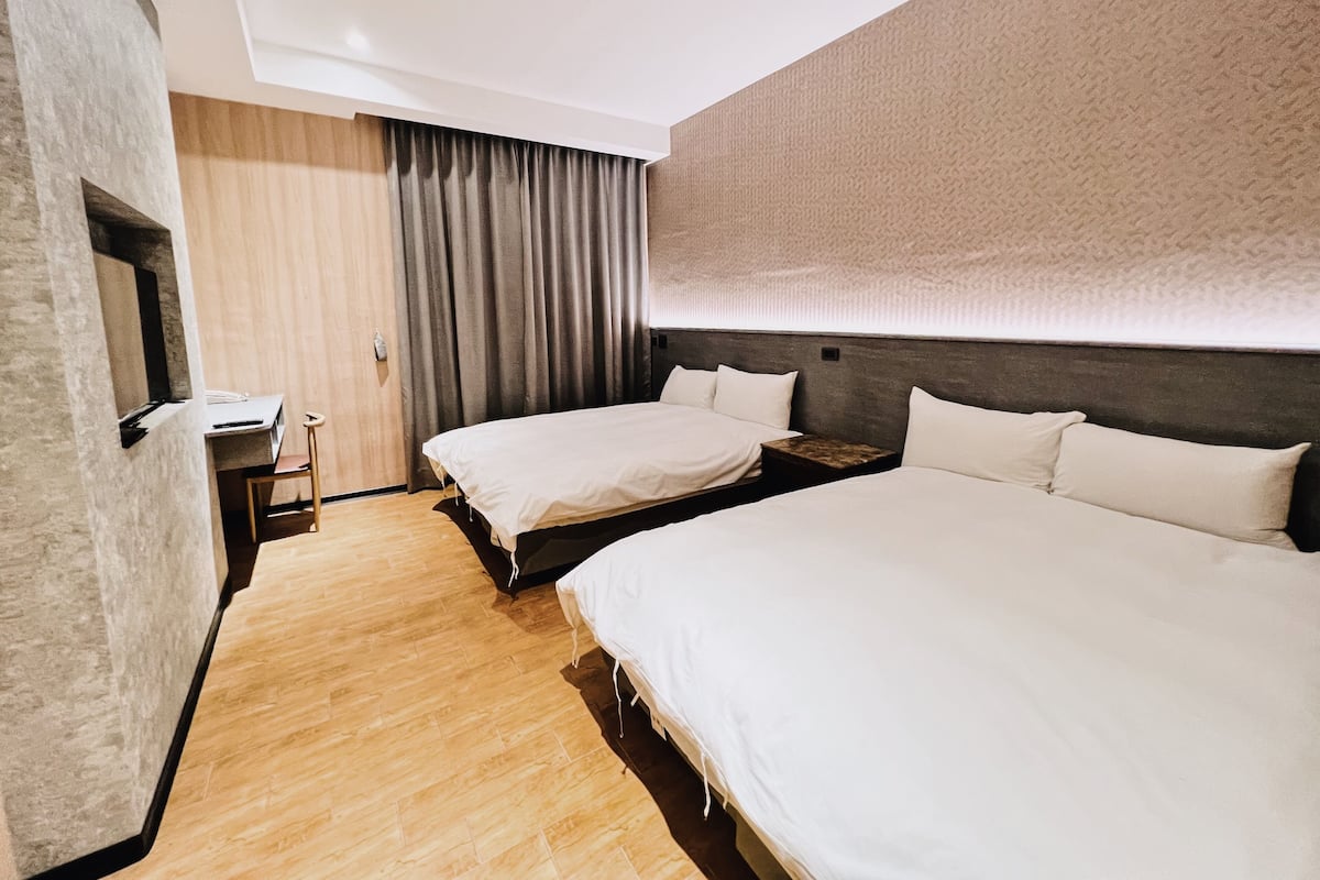 Habitación de hotel con dos camas, un escritorio, una silla, un armario y un ventanal con cortinas.