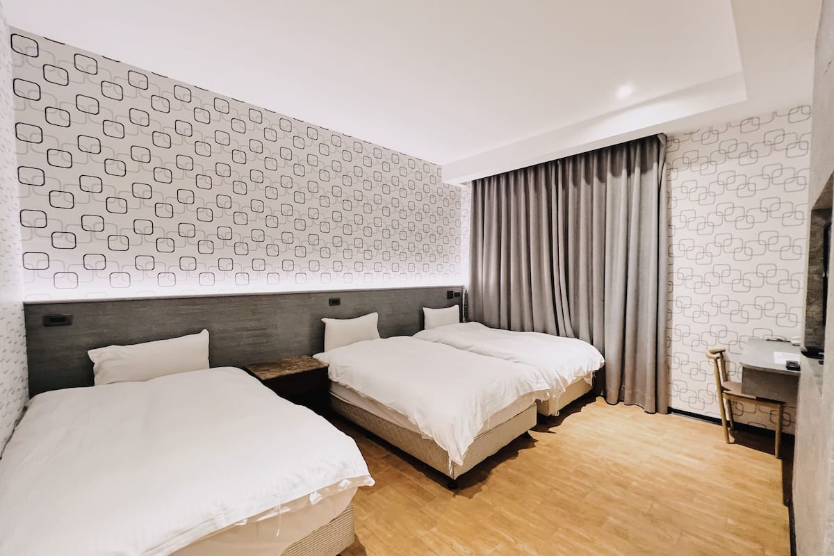 Habitación de hotel con dos camas, suelo de madera, pared estampada y una cortina.