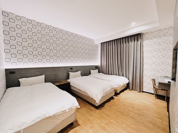 A hotel room with two beds, a wooden floor, a patterned wall, and a curtain.