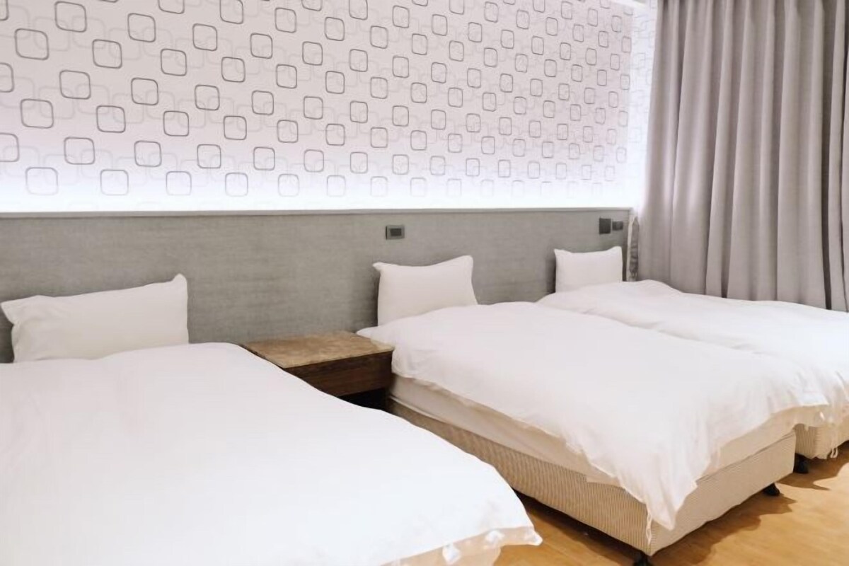 A hotel room with two single beds, a grey headboard, a patterned wall, and a window with curtains.