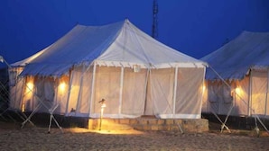 A row of white tents with a central light source, set on a sandy ground. - Riddhi Siddhi Resort (Jaisalmer)