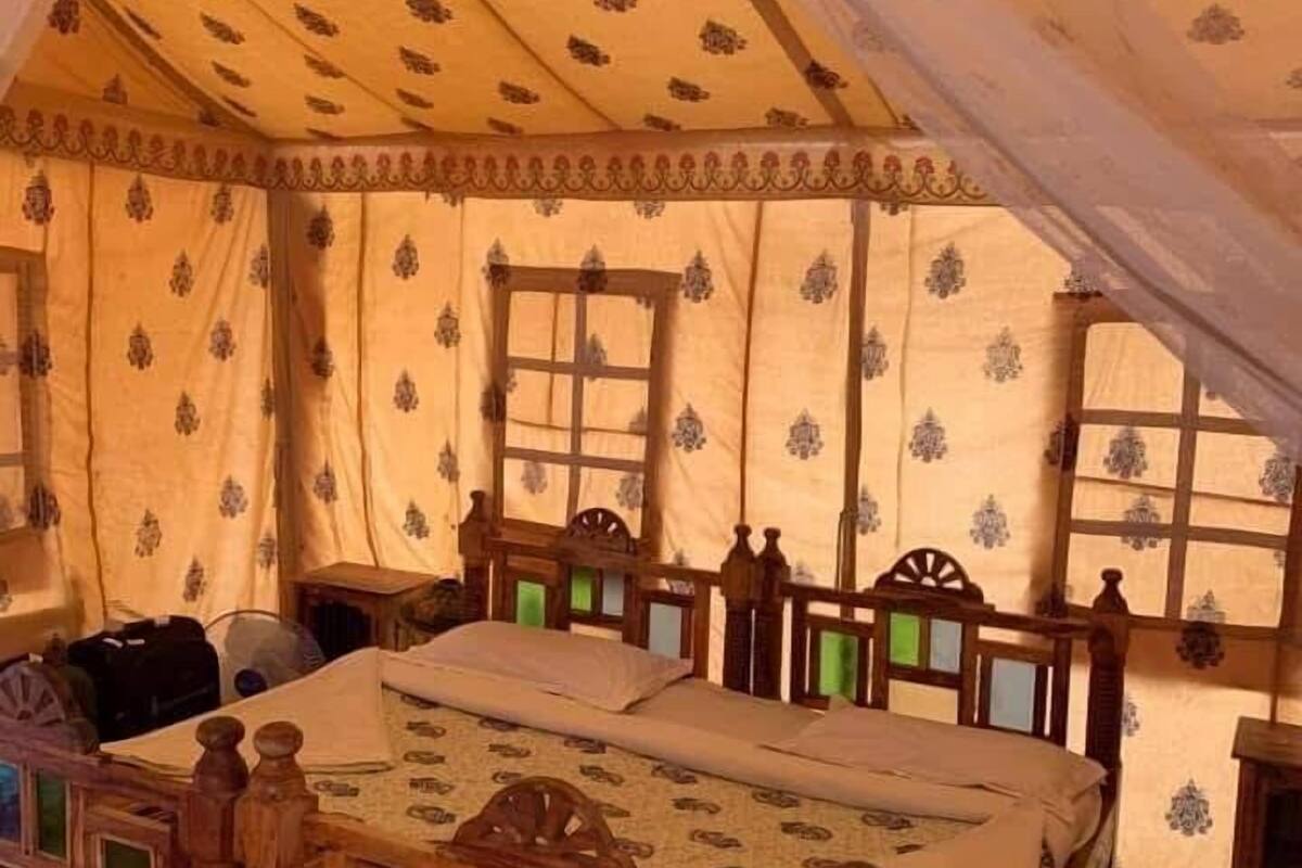 Habitación tipo tienda de campaña con cama, cabecero de madera y cortinas estampadas.