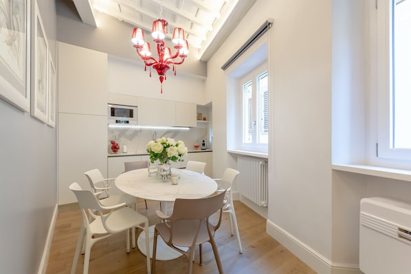 Une cuisine moderne avec des meubles blancs, un îlot central doté de sièges et un lustre rouge.