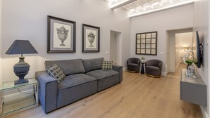 Ein modernes Wohnzimmer mit grauem Sofa, zwei gerahmten Kunstwerken, einem Glastisch, einer Lampe, einem grauen Sessel und einem kleinen Tisch mit Dekoration.